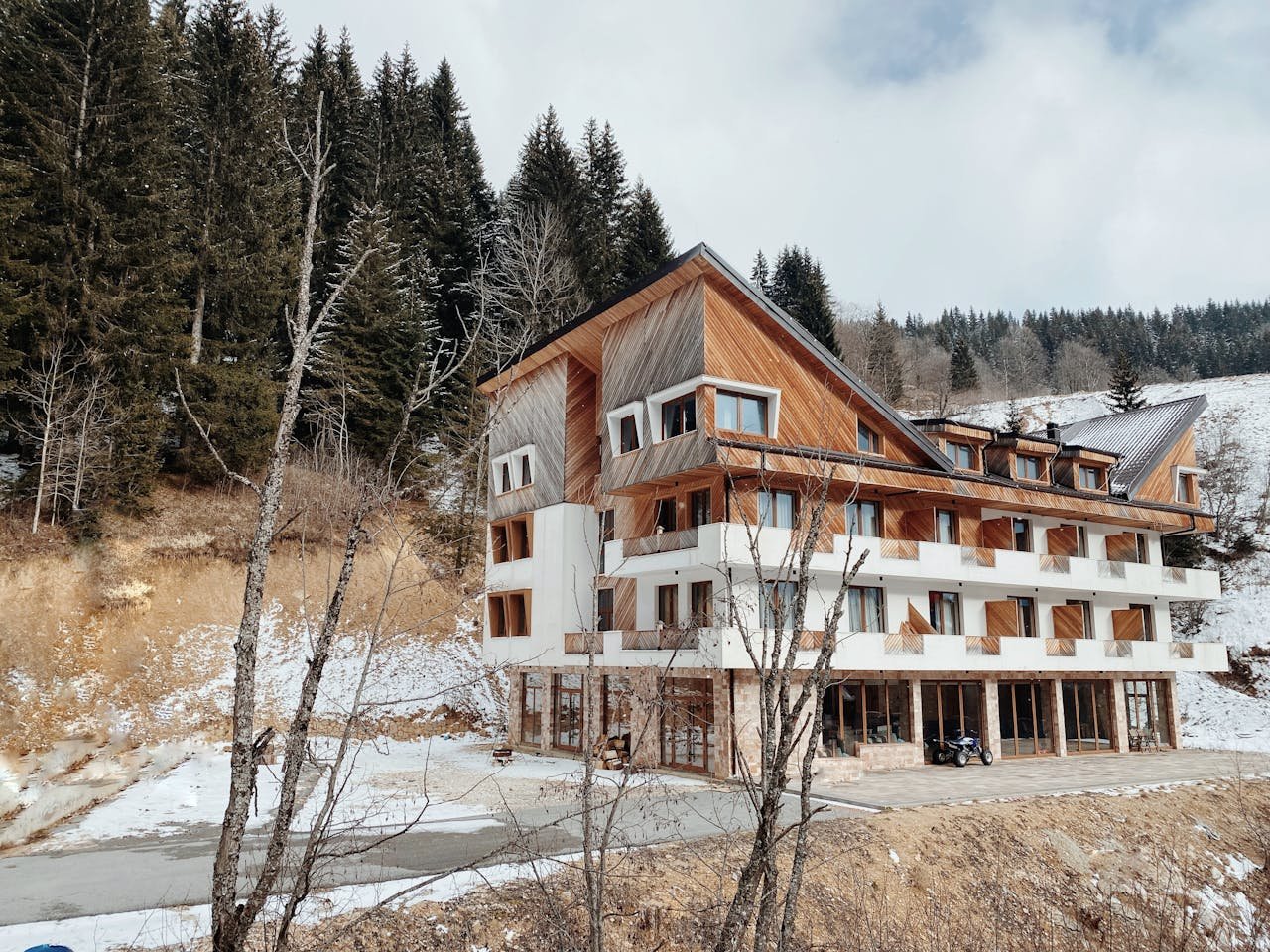 services-01 A large modern chalet nestled in a snowy mountain landscape surrounded by evergreen trees.