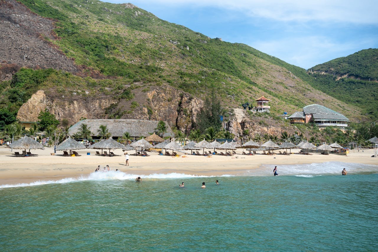 about-01 Scenic view of sandy beach with straw umbrellas washed by azure seawater and surrounded by rough grassy cliffs on hot summer day